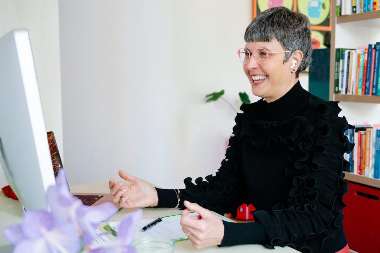 woman with short gray hair smiling in front of a computer monitor at her desk