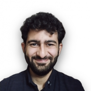 Headshot of Haseeb smiling at the camera. He has black hair and a short full-face beard. He wears a black shirt.