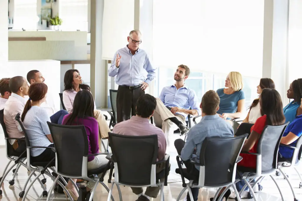 business people sitting is a circle with man talking to them for coaching