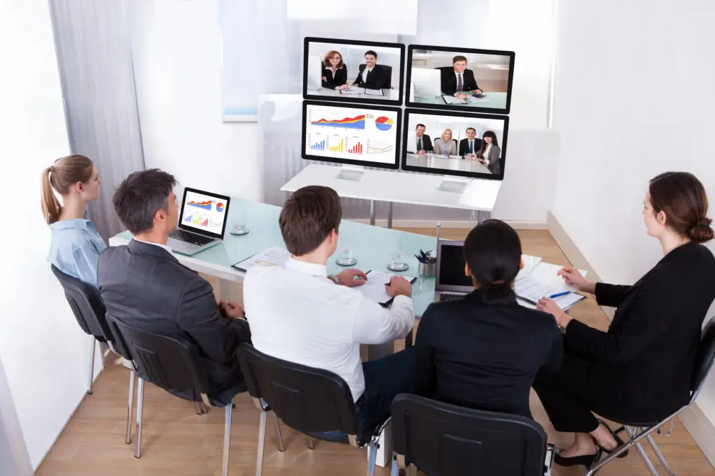 people sitting in a room at a table meeting with people on monitors executive coaching