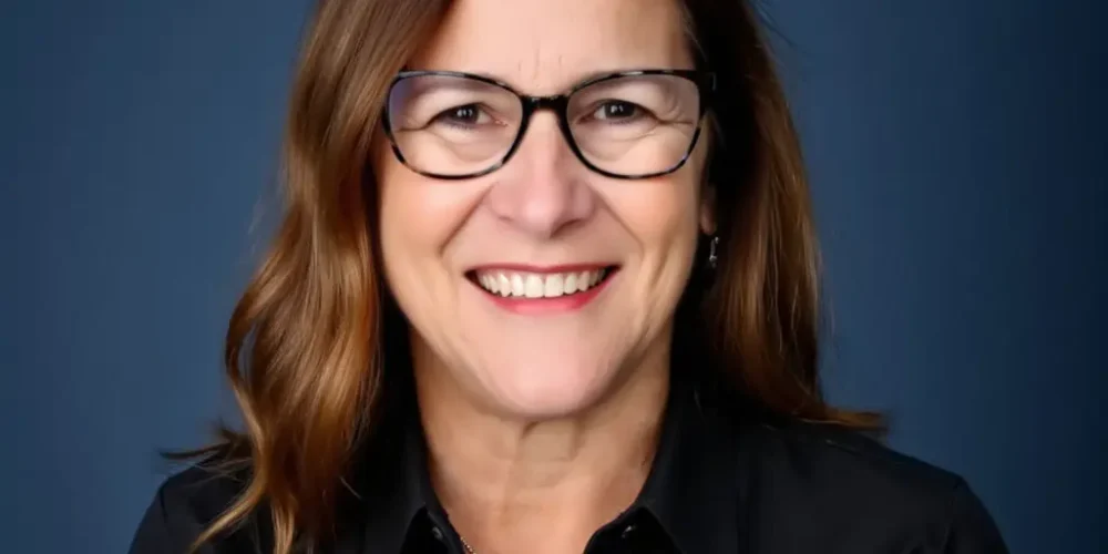 Headshot of Ellen smiling. She has medium brown hair just past her shoulders. She wears a black button up shirt and silver necklace.