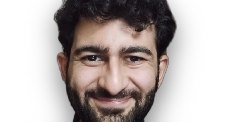 Headshot of Haseeb smiling at the camera. He has black hair and a short full-face beard. He wears a black shirt.
