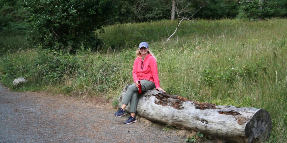 Cora Garvey sitting on a log outside near a trail