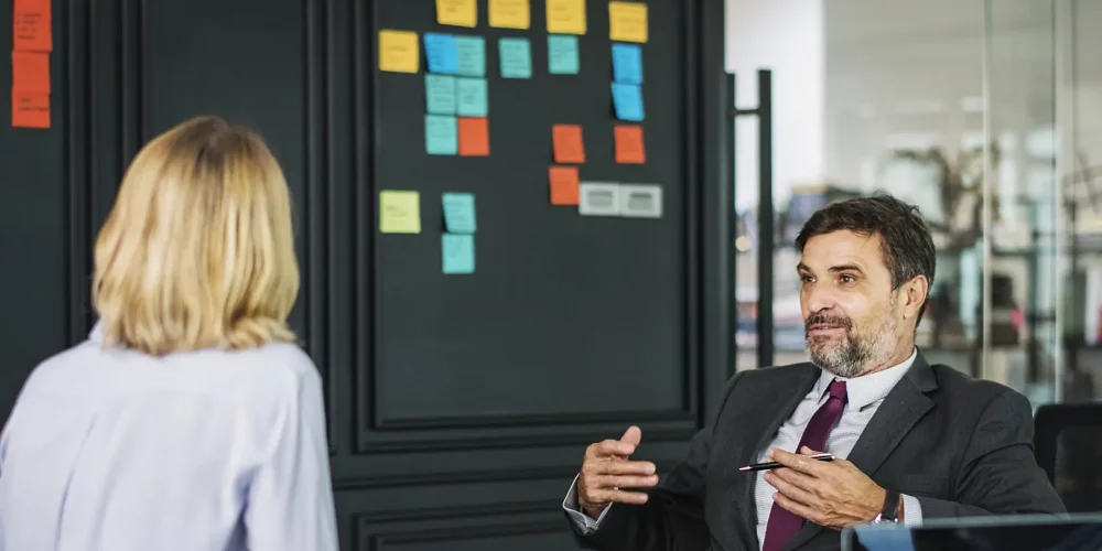 a man wearing a suit explains to a woman how to hire a coach.
